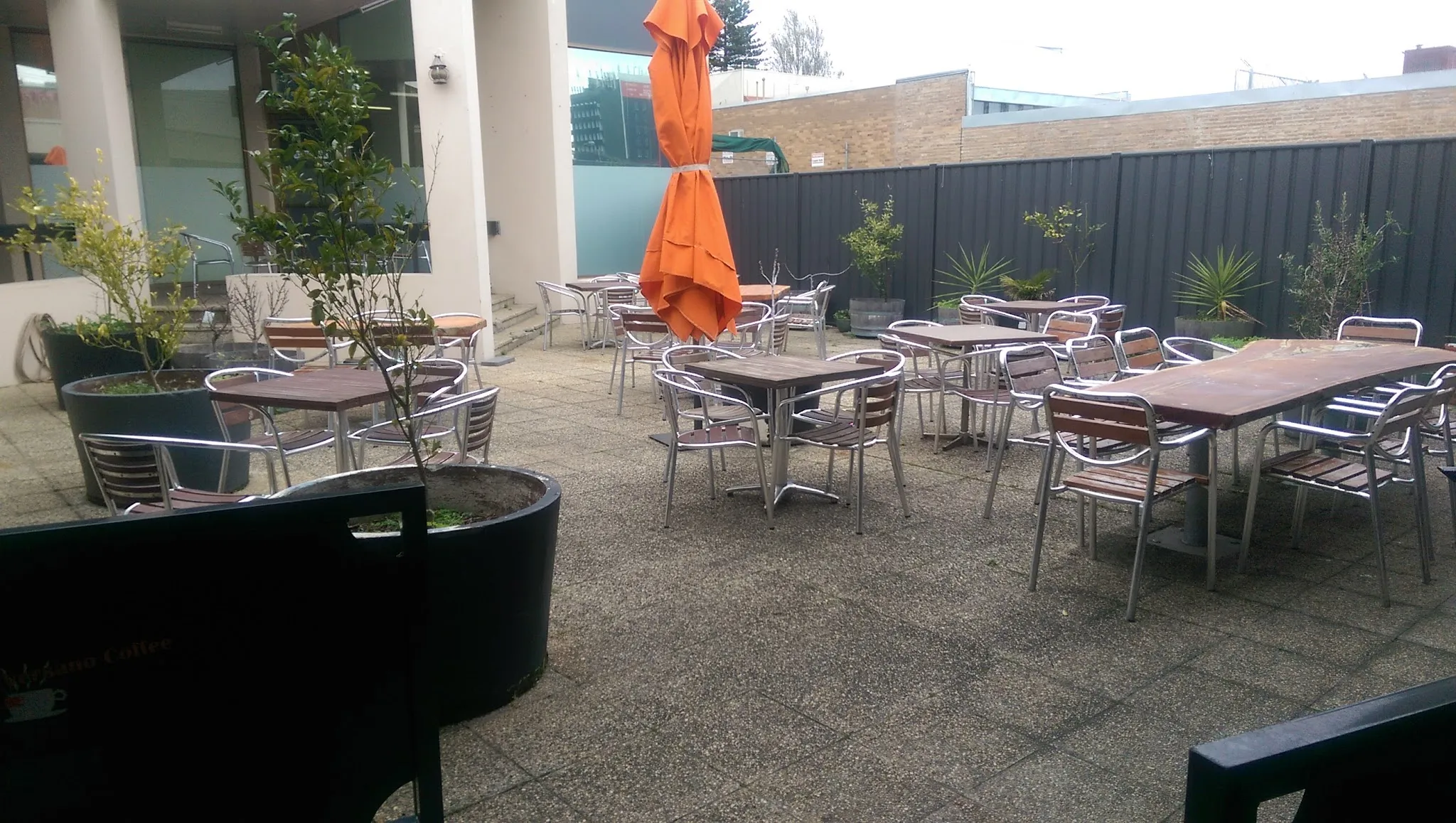 Trims outdoor courtyard with bistro tables, folded orange umbrella and potted plants