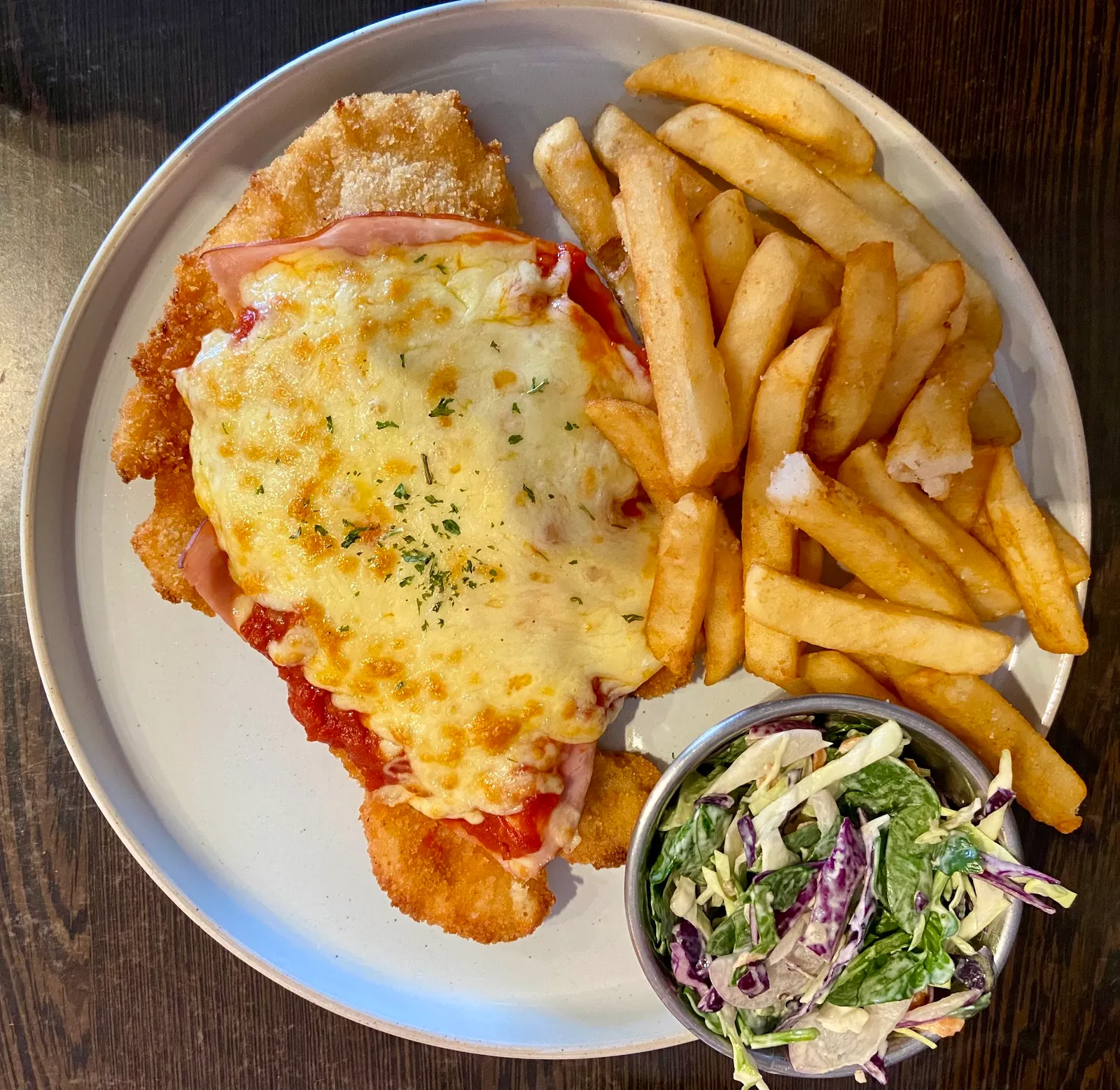 Chicken parma with melted cheese on white plate with chips and coleslaw