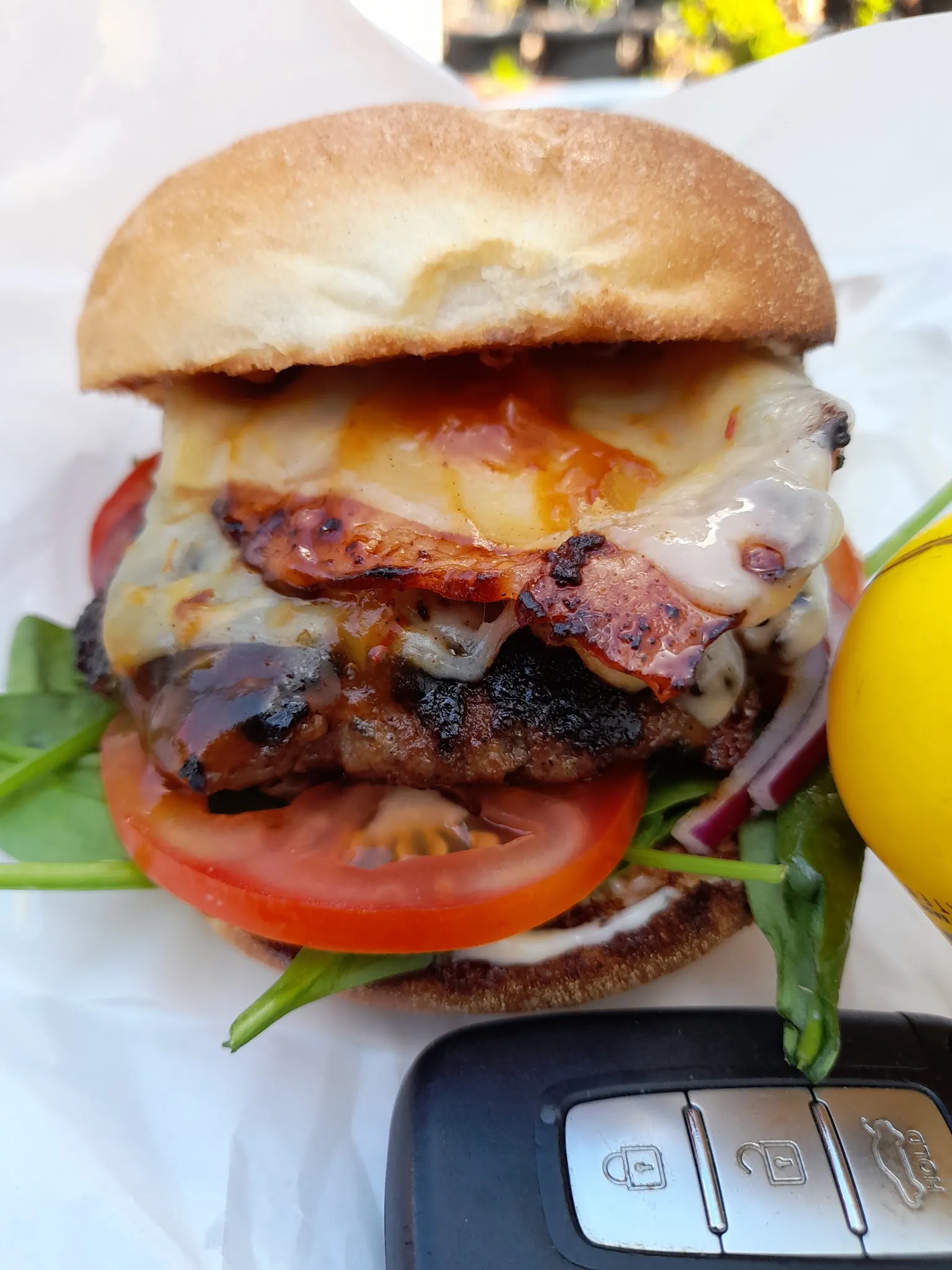 Gourmet burger with bacon, melted cheese, tomato and spinach on white paper