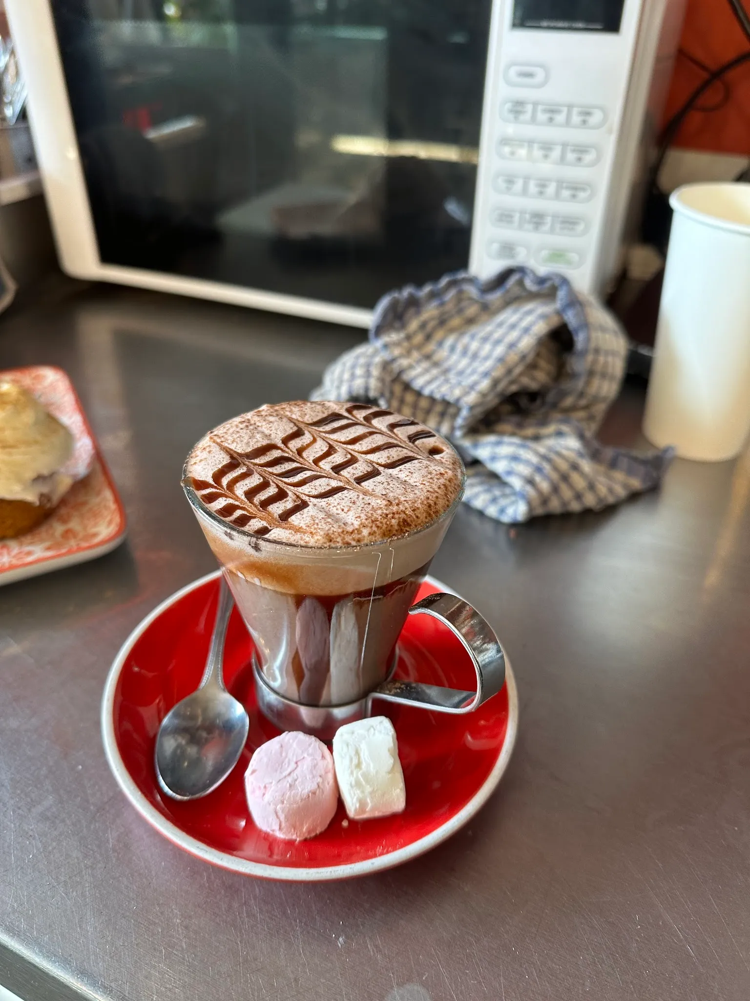 Hot chocolate with leaf cocoa art in glass mug with marshmallows on red saucer