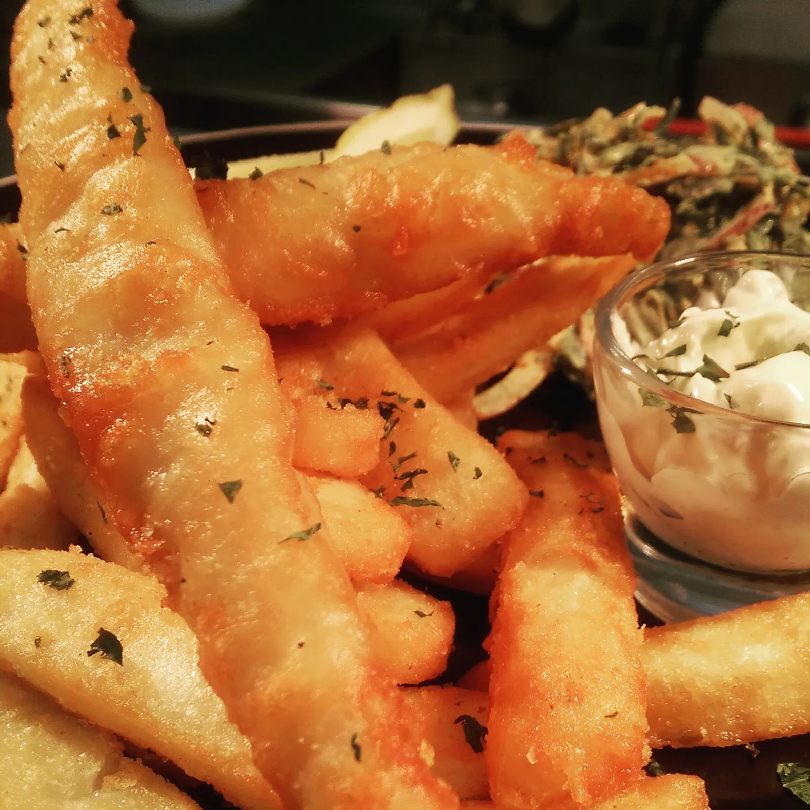 Beer-battered fish and chips with tartare sauce on dark plate