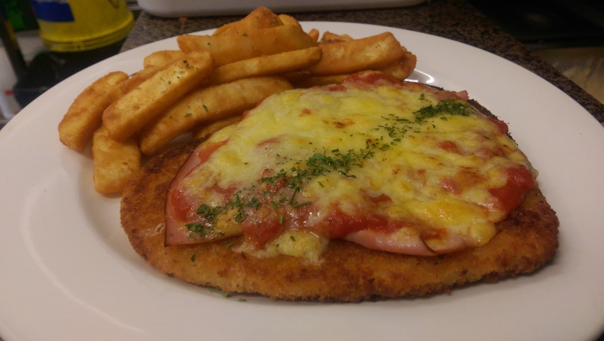 Chicken parma with melted cheese and chips on white plate