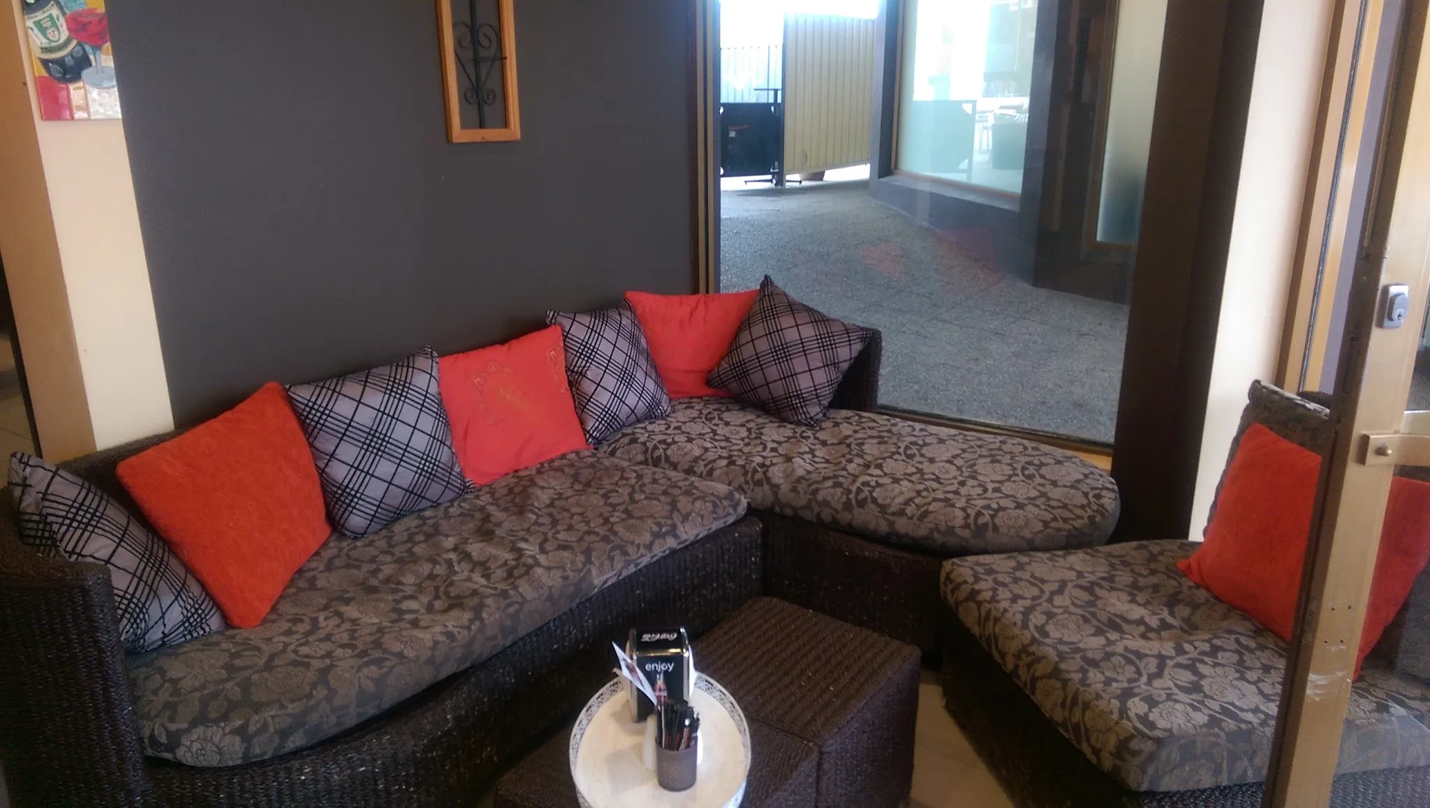 Trims lounge area with wicker sofa, red cushions and view to outdoor courtyard