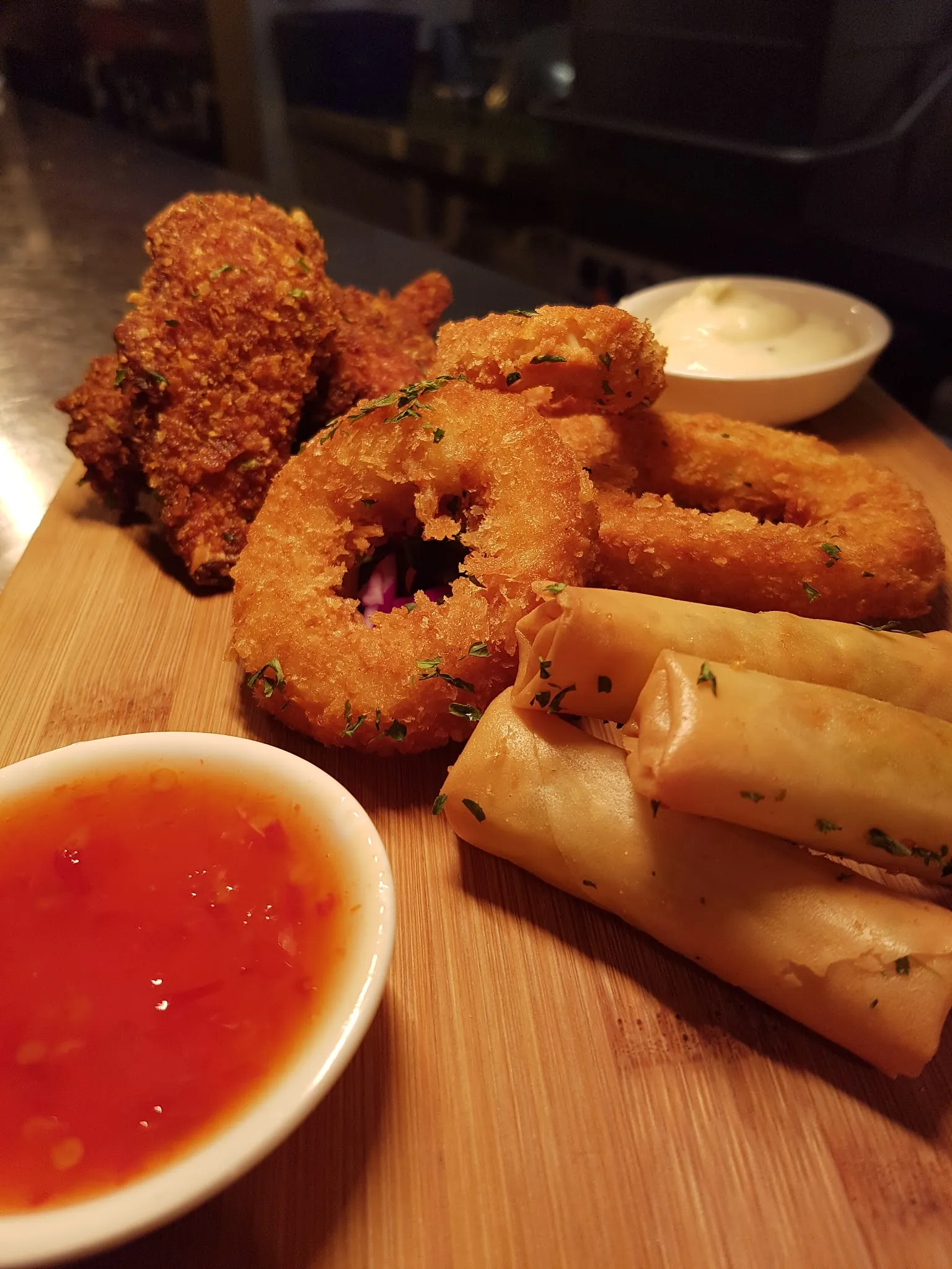 Share platter with chicken wings, onion rings and spring rolls with dipping sauces on wooden board