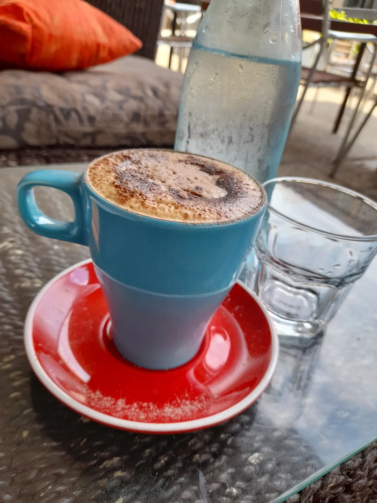 Cappuccino in blue mug on red saucer with Trims lounge and courtyard in background