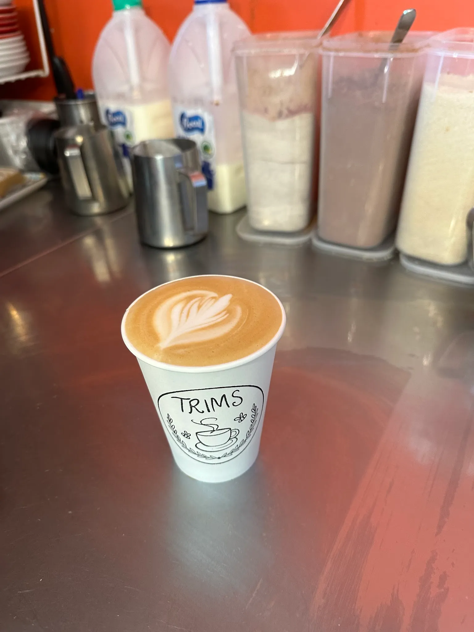 Trims branded takeaway coffee cup with latte art on stainless steel bench