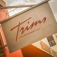 Trims Cafe Restaurant Bar hanging sign on terracotta wall exterior